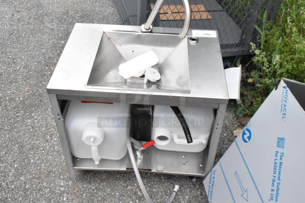 Stainless steel single bay sink with under-shelf storage. Visible hoses and containers. Slight wear, functional condition.