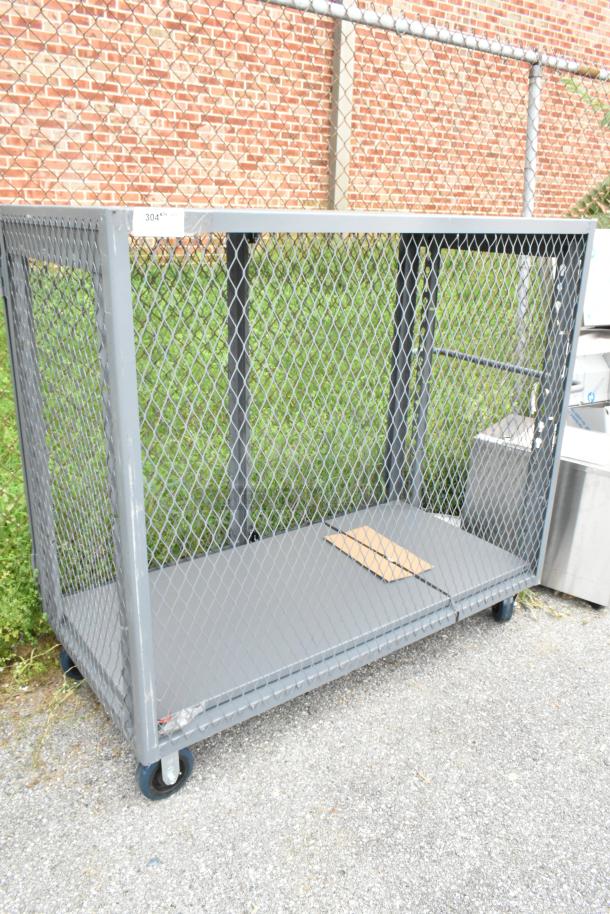 Gray metal cart with mesh sides on commercial casters, used condition. Ideal for transport and storage.