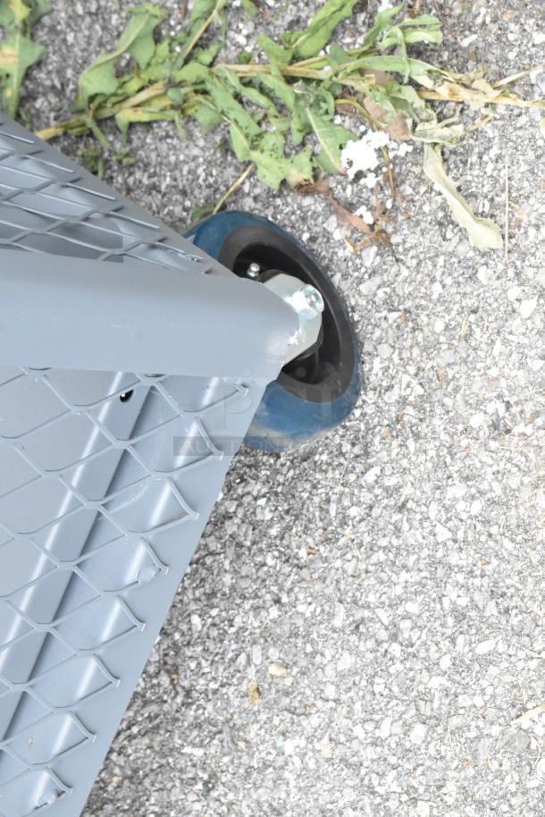 Gray metal cart corner with commercial caster, showing durable mesh design and solid wheel base, on concrete surface.