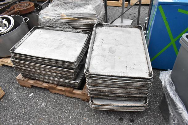 Pallet of used full-size metal baking pans stacked, showing signs of wear. Plates are on a wooden pallet outdoors.