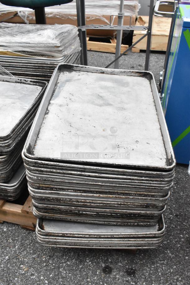 Pallet lot of used metal full-size baking pans stacked outdoors, showing signs of wear.