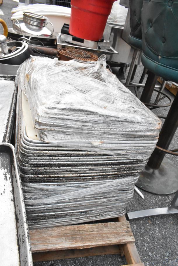 Pallet lot of metal full-size baking pans, wrapped in plastic, showing signs of wear. Ideal for bulk purchase.
