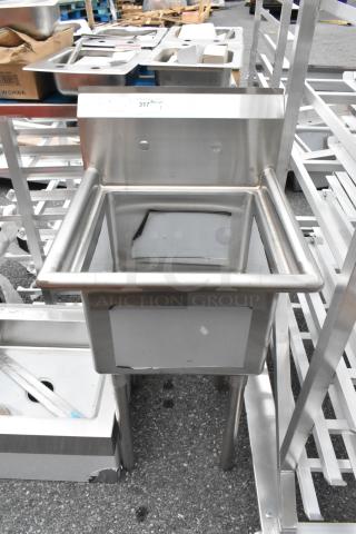 Stainless steel single bay sink, industrial design, with backsplash and sturdy legs. Slight wear visible, good condition.