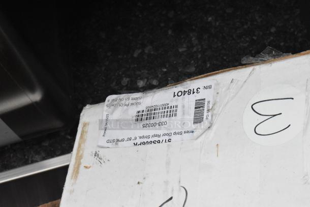 Cardboard box with shipping label and handwritten markings. Contains auction items like Table Top Thermo Form 3048 GRY WOOD and Steelton Work Table. Box condition suggests "scratch and dent" status.