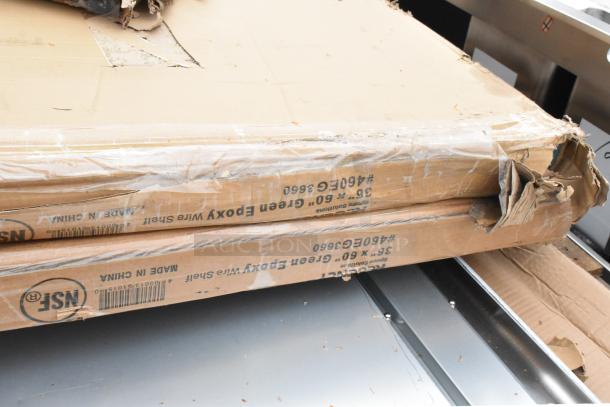 Stack of unopened, slightly damaged boxes labeled "36 x 60 Green Epoxy Wire Shelf" atop stainless steel work table.