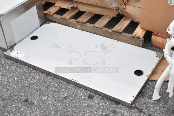 Brand new stainless steel panel with visible scratches and dents, on a pallet. Tag marked "323".