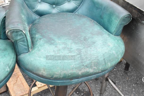 Set of 2 bar height chairs in teal leather with visible wear, tufted backrest, and metal legs. Sold as a pair.