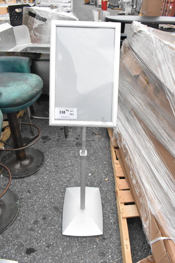 Freestanding white sign holder, silver frame, adjustable stand, displayed outdoors. Auction tag reads "338 TK QTY X2."