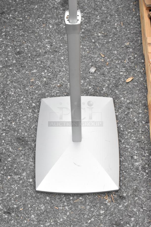 Base of a freestanding sign, metal, gray, triangular support, minor wear, on asphalt surface. No visible labels or markings.