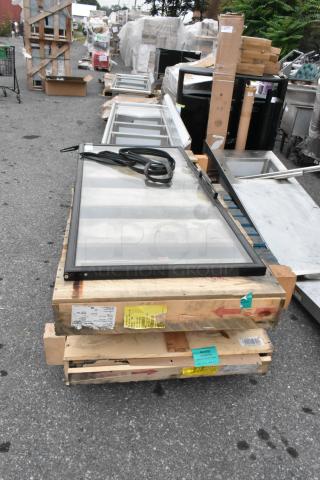 Three brand new scratch and dent doors, including a Slimline black 3-pane reflective door and a Slimline chrome 2-pane normal temp door, stacked on wooden pallets, with labels and markings indicating specifications.