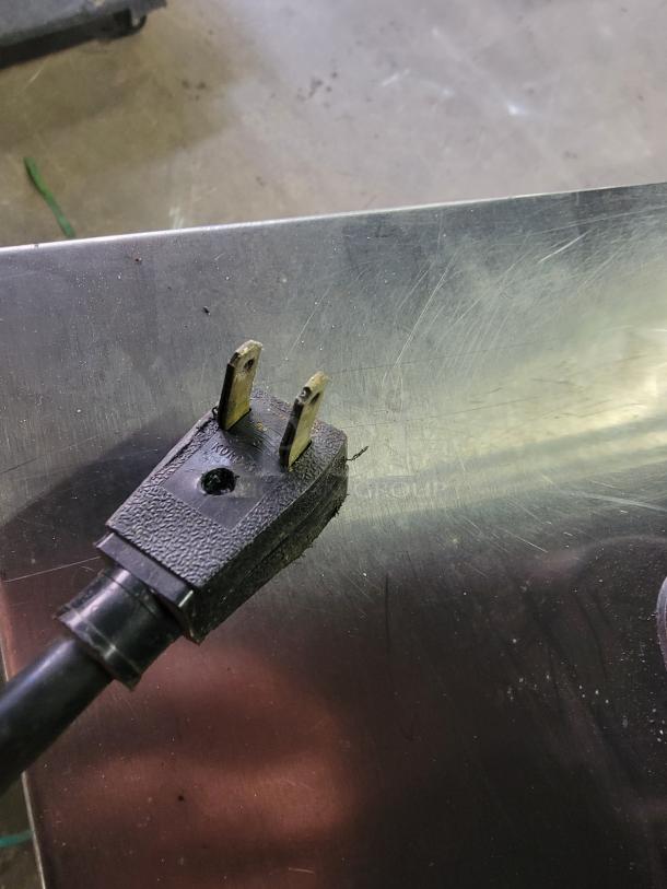 Power plug of True GDM-05 Countertop Merchandiser Refrigerator, showcasing standard prongs and cable condition on stainless steel surface.