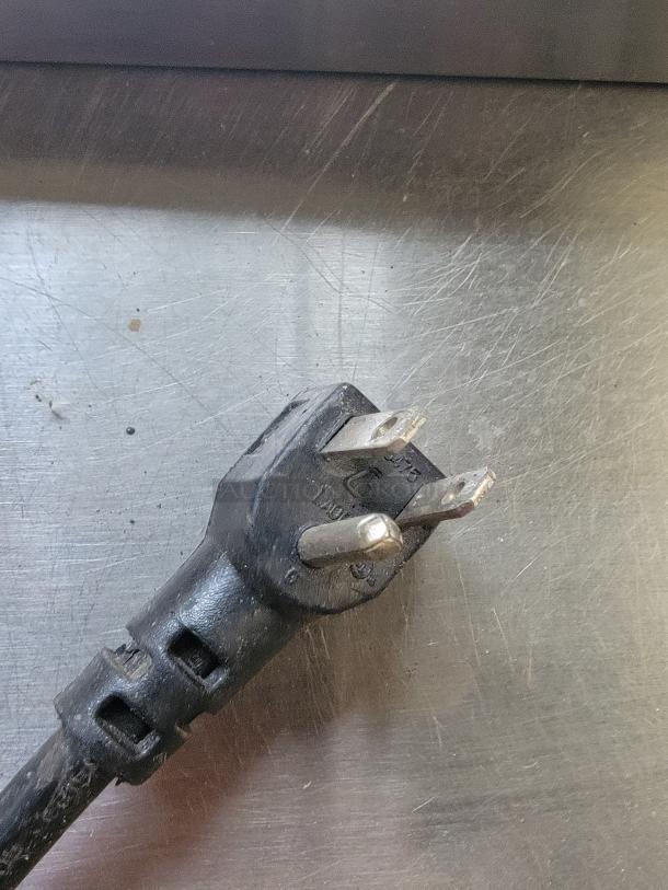 Close-up of a three-prong power plug on a stainless steel commercial surface, from a Continental Refrigerated Prep Table.