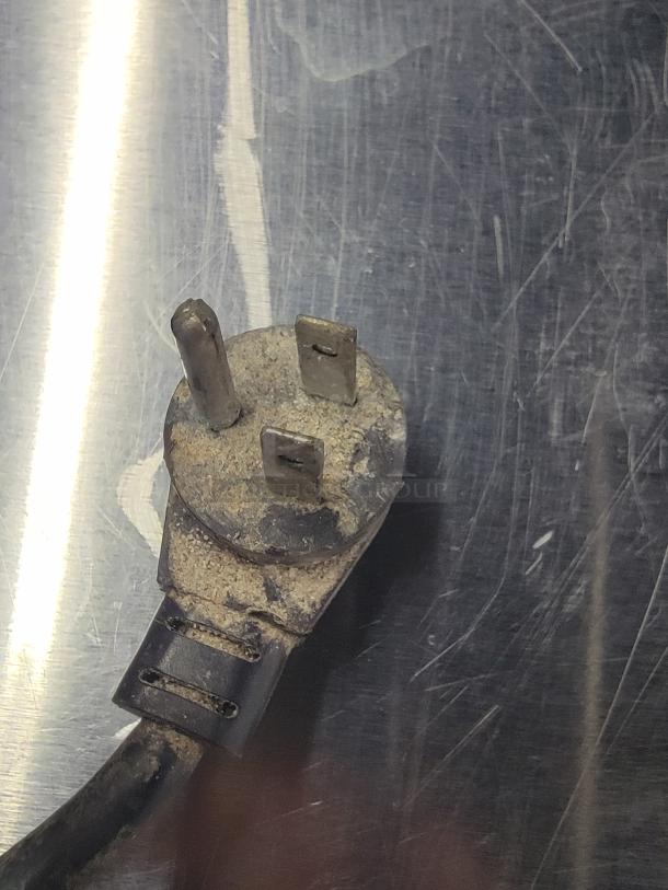 An old, worn power plug on a scratched metal surface, possibly part of a Manitowoc Delfield refrigerator.