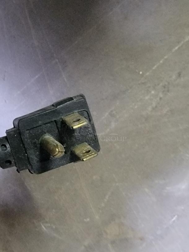 A close-up of a power plug for a Fagor FST-48-12 refrigerated prep table, showing three metal prongs.