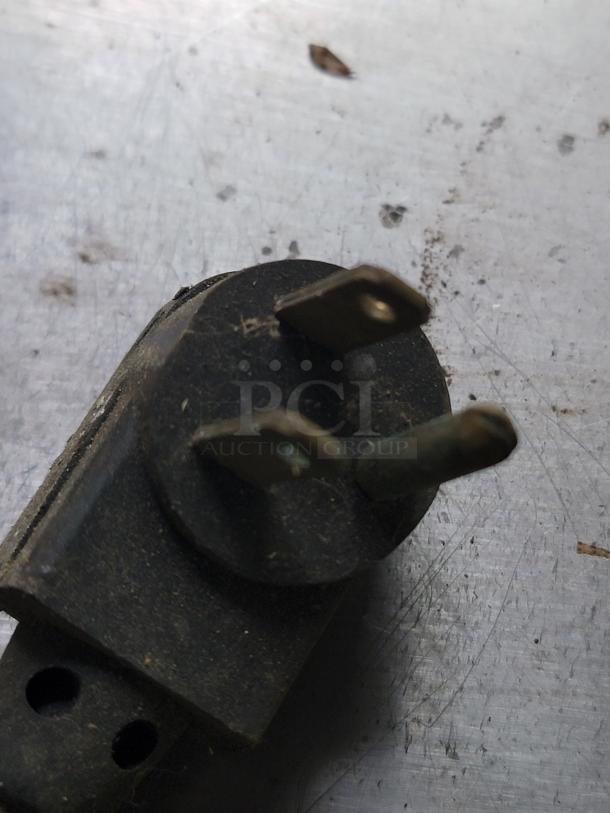 Old electrical plug on a scratched metal surface, featuring two prongs with visible wear and corrosion.
