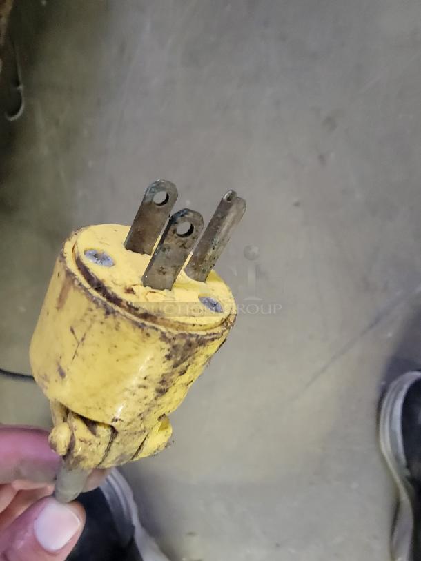 Yellow industrial plug with three prongs, showing signs of wear and rust.