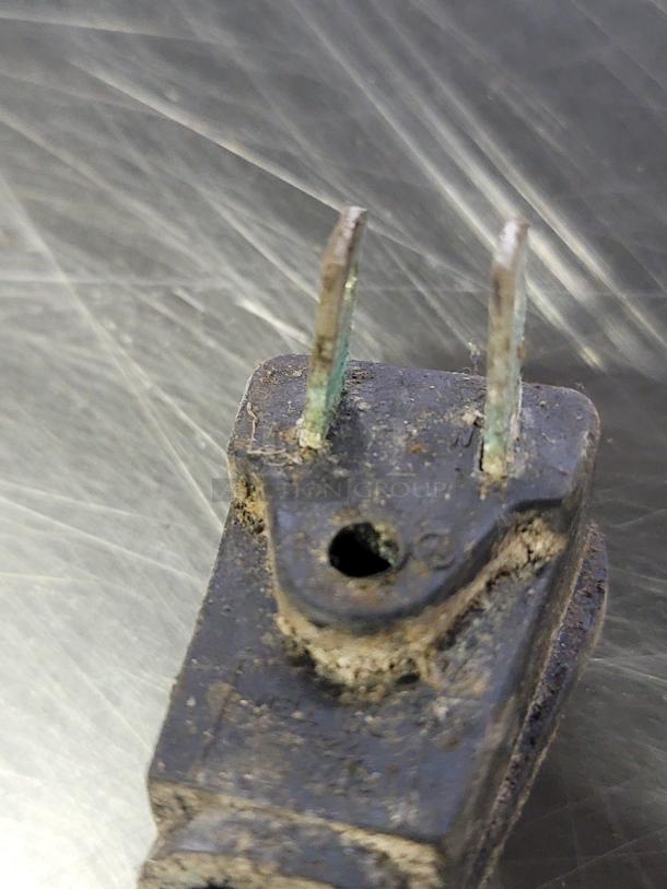 Corroded electrical plug with visible wear, detached from its appliance. Appears damaged and in poor condition.