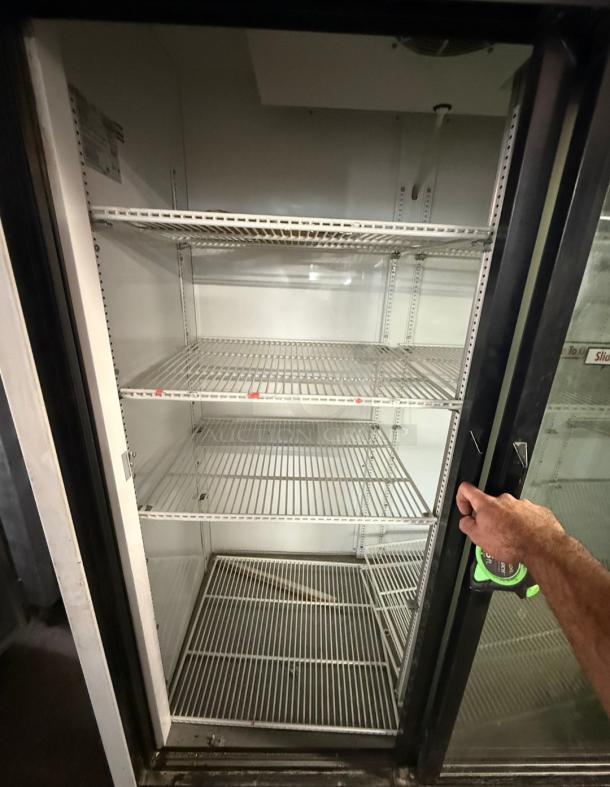 TRUE GDM-69 commercial refrigerator with three glass sliding doors. Features multiple shelves, suitable for retail display. Clean and spacious interior.