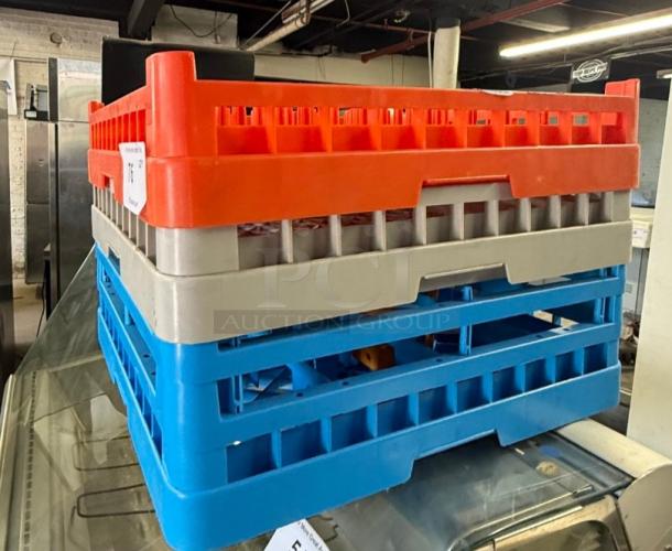 Three commercial dishwasher racks, 19x19 inches, in red, gray, and blue, stacked and ready for use in a restaurant.