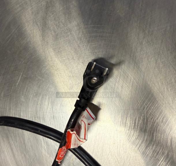 Power cord plug for Bison BUR-27 Commercial Refrigerator against a metal surface, showing condition and design.