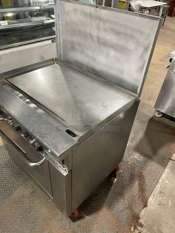 Migali commercial stainless steel flat griddle range/oven combo with backsplash, wired oven racks, and casters.