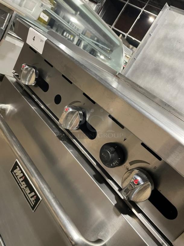 Migali commercial stainless steel natural gas flat griddle range/oven combo with backsplash, wired racks, casters, visible control knobs.