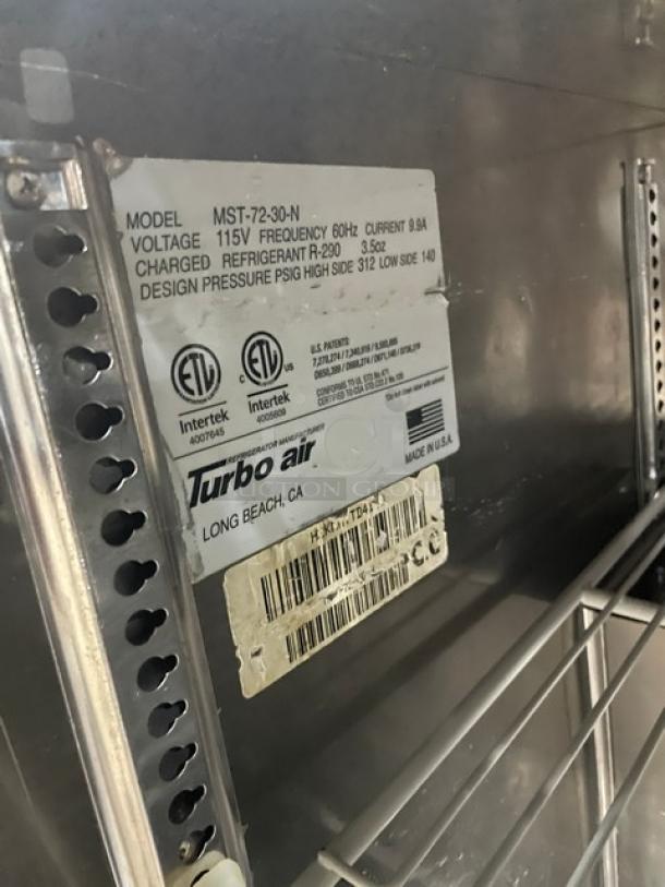 Turbo-Air MST-72-30-N commercial stainless steel 3-door refrigerated prep table. Features poly coated wire rack, 115V. Visible labels indicate model and electrical specifications.