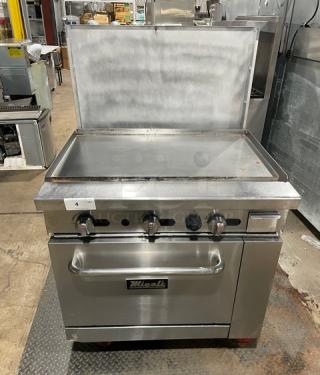 Migali commercial stainless steel natural gas flat griddle range/oven combo with backsplash, wired oven racks, on casters.