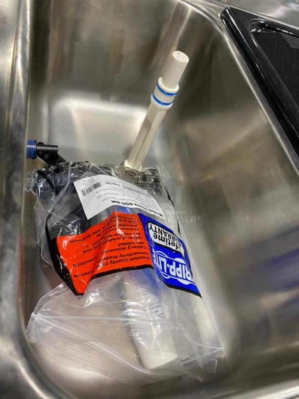 Commercial stainless steel sink with a Ripp-Ur 1 cleaning product bag and plumbing items inside.