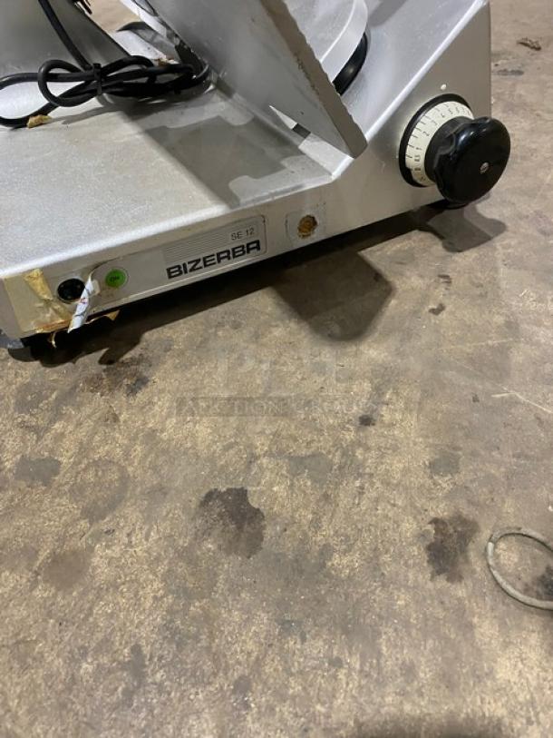Bizerba commercial electric deli slicer on legs, model SE12, 120V, featuring a dial control. Visible wear on the casing.