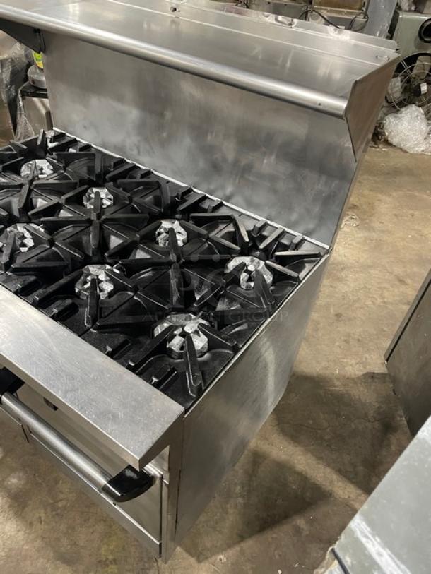 U.S. Range stainless steel 8-burner range and double oven combo, with backsplash, overhead salamander shelf, wired oven rack, on legs.