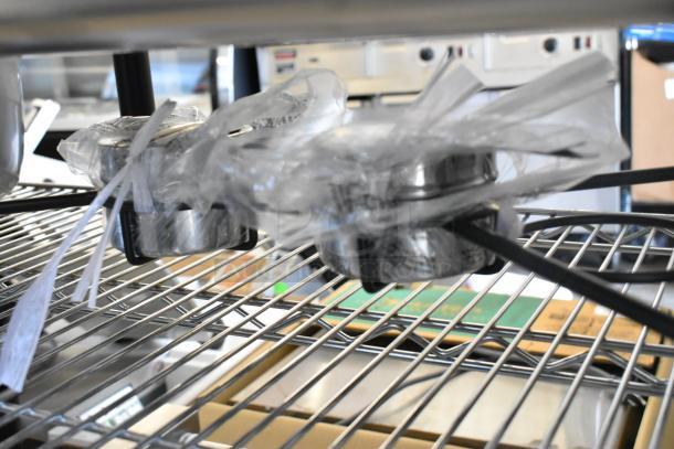 Brand new stainless steel chafer with minor scratches and dents, wrapped in protective plastic on a metal rack.