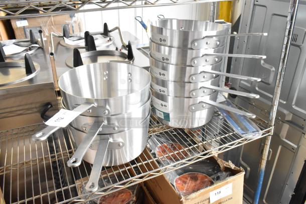 8 new Winco ASP-10 10 qt aluminum saucepans with solid handles, minor dents, on metal shelf. Tags indicate model.