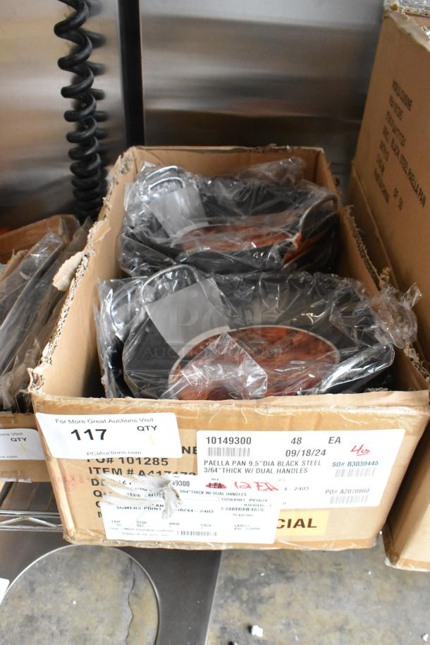 Box of 12 brand new scratch and dent Vollrath 9.5" paella pans, model 10149300, with black steel and dual handles.