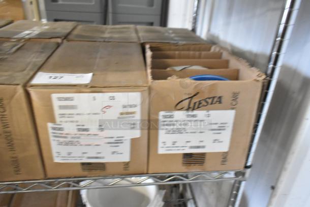 Boxes of 4 brand new Fiesta ceramic bowls, labeled "scratch and dent," on a shelf. Fragile labels visible.