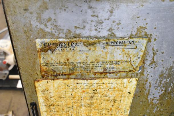 Close-up of a worn Frymaster FM245ESC label on a commercial fryer, indicating industrial use and installation details.
