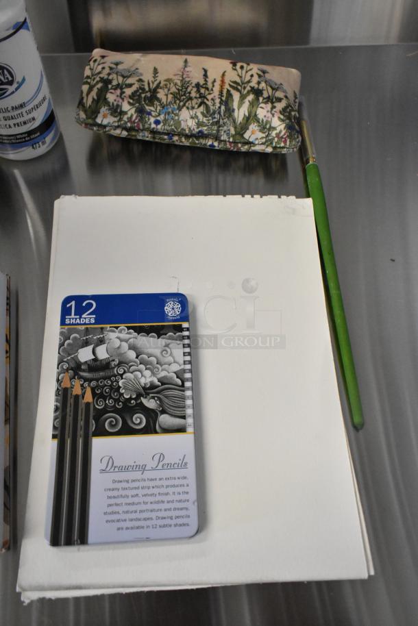 Lot of art supplies including a drawing pad, 12-shade drawing pencils, acrylic paint, brushes, and a floral pencil case.