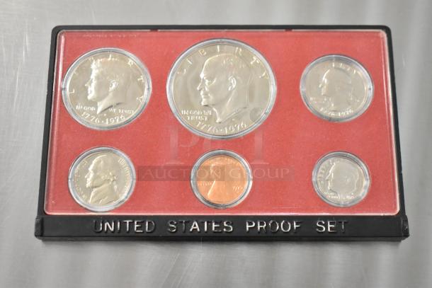 United States proof coin set, six coins in a case, dates 1776-1976 visible, coins in mint condition, red background.