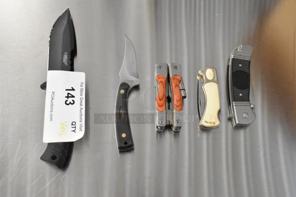 Five various pocket knives, including Schrade 1520T, CRKT R2301, Camillus 440, on a metal surface; auction tag stating "143 QTY 5" visible.