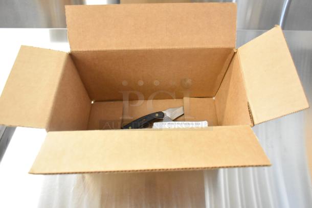 Open cardboard box with five assorted pocket knives, including Schrade 1520T, CRKT R2301, and Camillus 440 models.