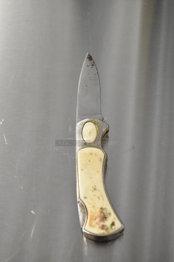 Vintage pocket knife with cream-colored handle. Notable wear on blade and handle. Part of a set of five knives.