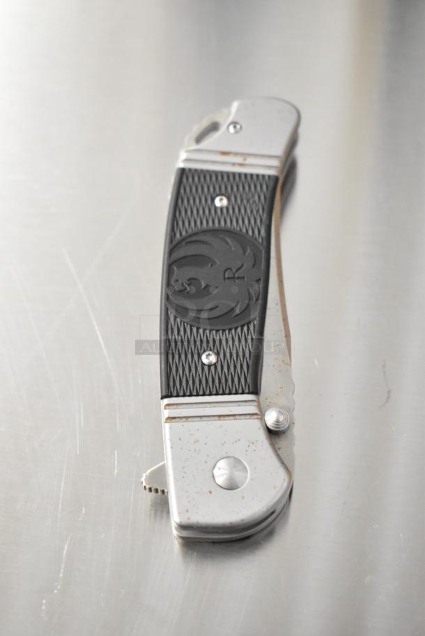 Rugged pocket knife with silver and black handle, featuring an engraved emblem. Slight rust on metal parts.