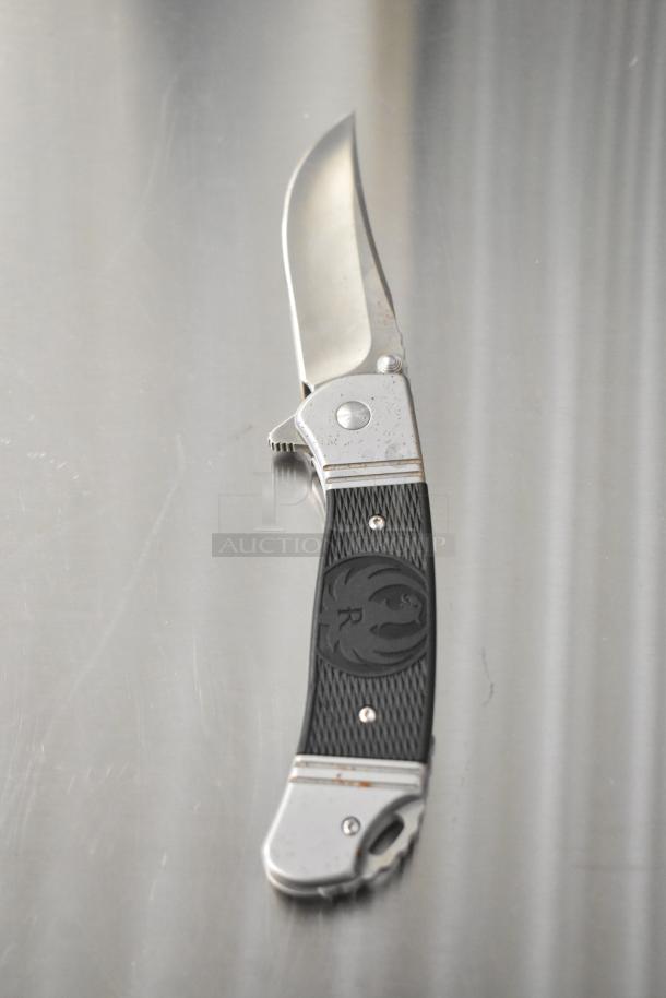 Schrade 1520T pocket knife, silver and black handle, stainless steel blade, visible wear marks, R emblem on handle.