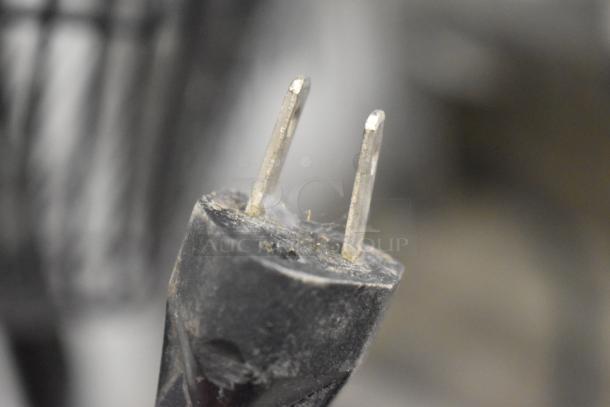 Close-up of the plug from a Dayton 2LY97B black metal floor fan, showing minor dust, suitable for indoor use, 120 volts.