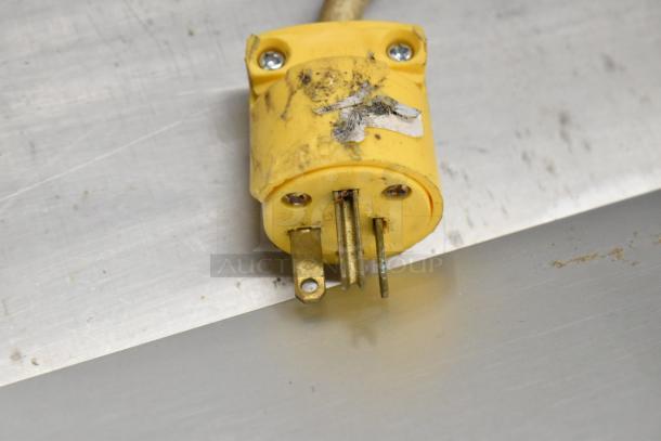Yellow electrical plug with visible wear and a partially peeled label, likely part of a larger appliance setup.