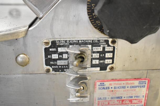 Globe 775 stainless steel commercial meat slicer with blade sharpener, 115V, 1 phase. Model tag showing technical specs.