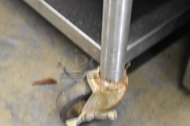Stainless steel equipment stand with metal undershelf on commercial caster, showing signs of wear and rusting casters.