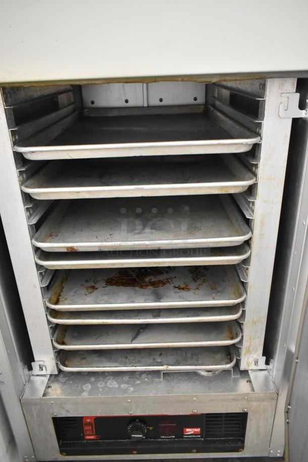 Metro FlavorHold C199 metal commercial heated holding cabinet with trays, on casters. Visible wear on interior surfaces.