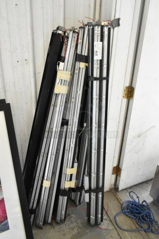 Bundle of 45 tube lights stacked against wall. Includes wiring and connectors. Auction tag with "210" visible.