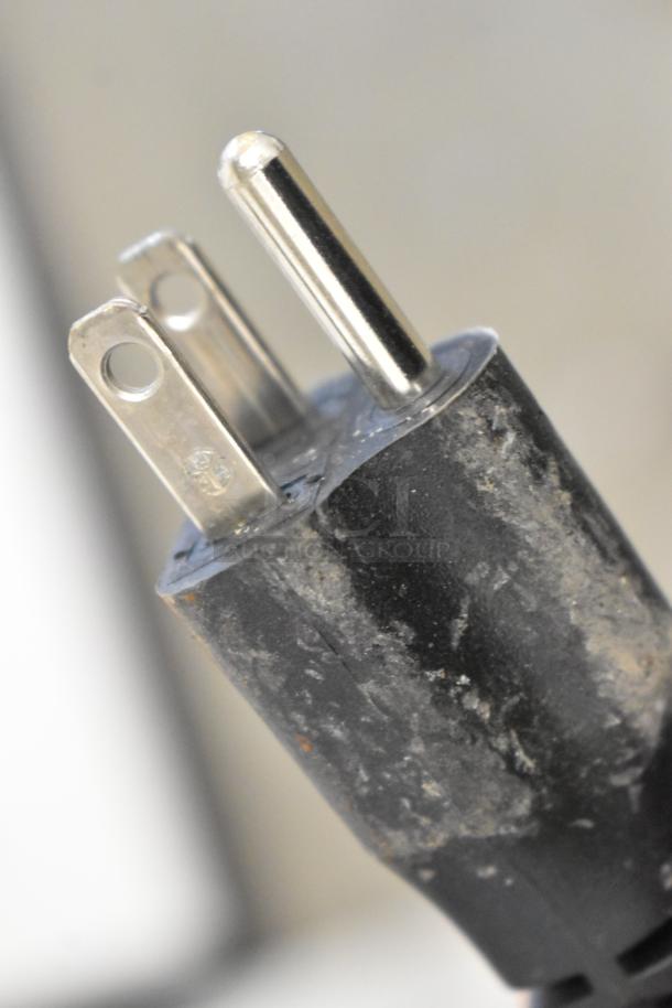 Close-up of a worn 3-prong plug, possibly from a Globe C10 meat slicer, showing scratches and texture details.